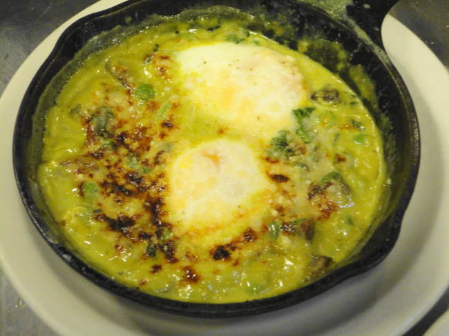 Two eggs broiled in  a skillet with watercress, spring peas, mushrooms, watercress cream and parmesan.