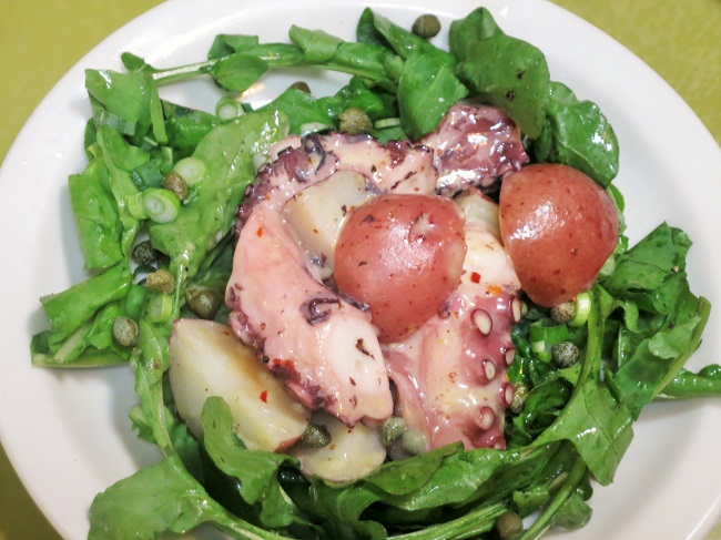 Octopus in the style of the Camargue, served warm tossed with aioli, red potatoes, capers and red chili flake, on a bed of arugula and green onions